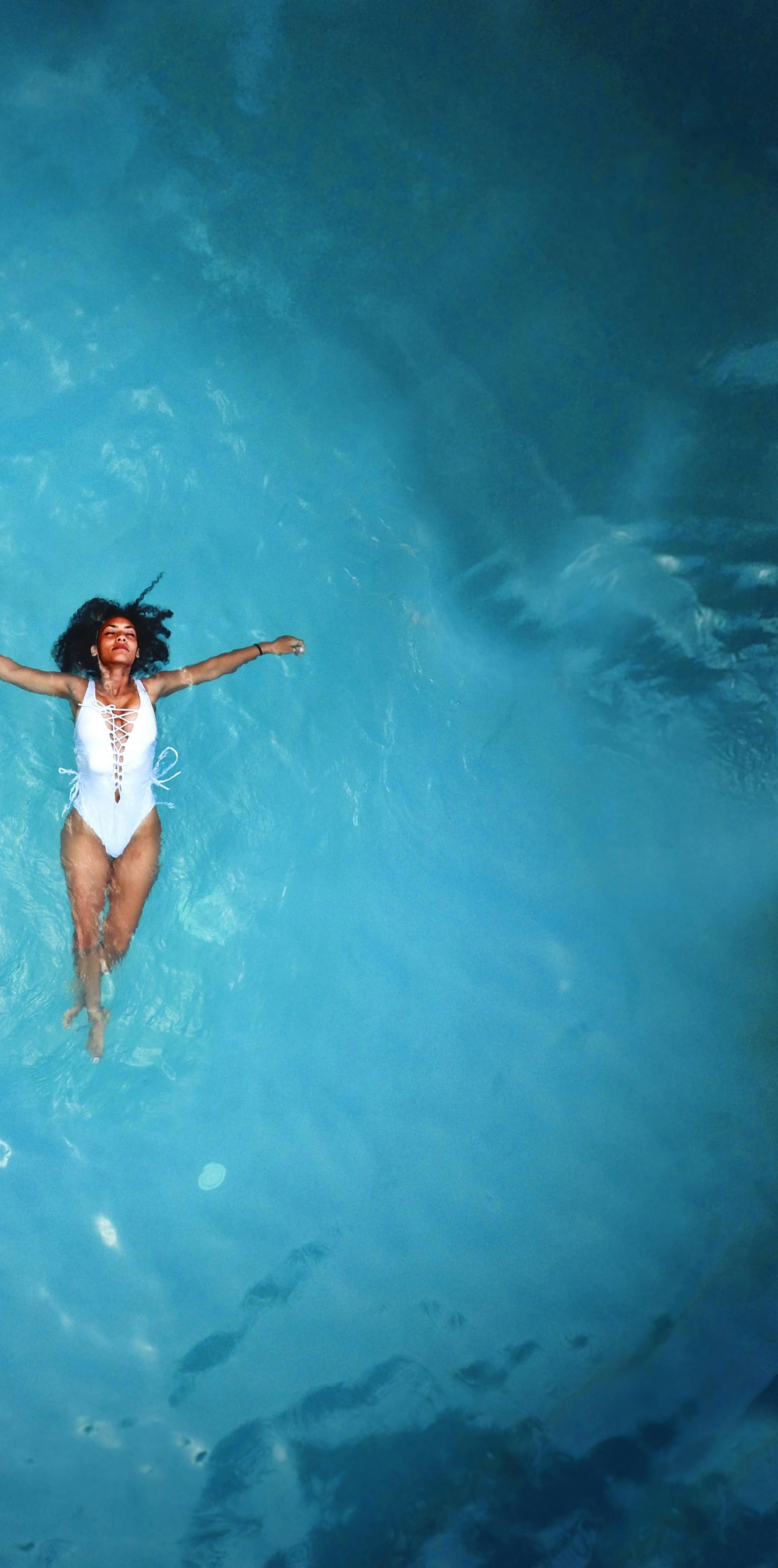 An African American woman in a swimsuit floats peacefully in a clear blue swimming pool.