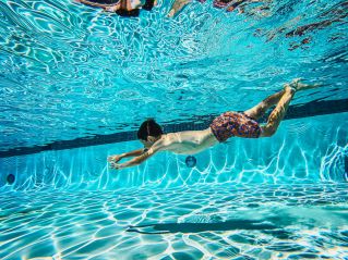 A child swimming underwater in a pool, showcasing vibrant sunlight patterns on the water surface.